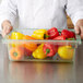 A chef in a white coat holding a Carlisle green food storage box of peppers on a school kitchen counter.
