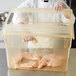 A chef holding a Carlisle yellow plastic food storage container filled with raw chicken meat.