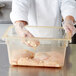 A person in gloves putting raw chicken in a Carlisle yellow plastic food storage container.