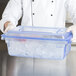 A person holding a Carlisle blue plastic food storage box filled with ice cubes.