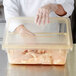 A person in gloves holding a Carlisle yellow plastic food storage container with raw chicken.