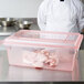 A chef in a white coat and pink gloves using a red Carlisle food storage box to hold raw meat.