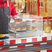 A person in a red shirt and apron using a Carnival King hot food display case to prepare hot dogs and french fries.