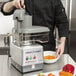 A man in a black coat using a Robot Coupe commercial food processor with a stainless steel bowl to chop peppers.