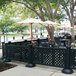 A black Grosfillex resin patio fence with white umbrellas and tables.
