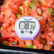 A purple Taylor digital pocket probe thermometer resting on a pile of diced tomatoes.