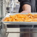 A person holding a tray of french fries in a Hatco Flav-R-Savor countertop hot food display warmer.