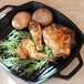 A black faux cast iron grill pan with chicken legs and mushrooms.