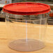 A clear plastic Carlisle food storage container with a red lid.
