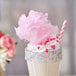 A milkshake topped with pink cotton candy and sprinkles.