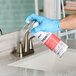 A person wearing blue gloves spraying Noble Chemical Impact disinfectant on a bathroom sink.