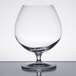 A Stolzle brandy snifter with a clear liquid inside on a table.