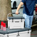 A person in a blue shirt carrying a white CaterGator outdoor cooler.