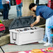 A large white rotomolded outdoor cooler with a black lid, filled with bottled drinks.