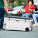 A person pushing a white CaterGator cooler on wheels.