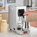 An automatic pourover milk steamer with a digital display, shown steaming milk in a stainless steel pitcher.