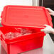 A hand placing a red Vollrath Traex food storage box lid on a red box.