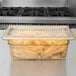 A clear plastic Cambro H-Pan lid on a glass container of french fries.