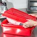 A person holding a red Vollrath food storage container with meat inside.
