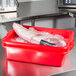 A red Vollrath Color-Mate food storage container with a piece of meat in ice.
