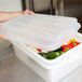 A person holding a Vollrath Traex clear plastic lid over a food storage container with vegetables inside.