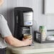 A person holding a cup of coffee in front of a Hamilton Beach BrewStation coffee maker.