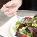 A hand holding a Oneida Rosewood stainless steel salad fork over a plate of salad.