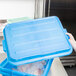 A person holding a Vollrath blue plastic container lid over food.