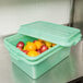 A green Vollrath food storage container filled with fruit on a counter.