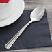 A Oneida Unity stainless steel teaspoon on a napkin next to a cup on a table.