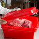 A person in a white shirt holding a red Vollrath Traex food storage box filled with meat.
