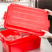 A woman using a Vollrath red plastic container with the lid open to store food.