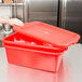 A hand holding a red Vollrath Traex food storage container with a lid.