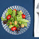 A Fineline clear plastic plate with a salad of lettuce, tomatoes, and croutons with a fork and knife.