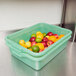 A green Vollrath Traex food storage container full of fruit on a counter.