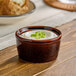 A brown porcelain ramekin filled with a creamy topping and garnished with chopped green onions.