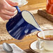 A blue porcelain creamer being used to pour milk into a cup of tea.