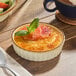 A vanilla bean creme brulee served in a white porcelain souffle dish, garnished with orange slices and a mint sprig.