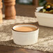 A white Acopa porcelain ramekin filled with brown sauce on a table.