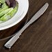 A Oneida stainless steel dinner knife on a plate with a salad.