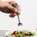 A hand holding a Oneida Unity stainless steel salad fork over a bowl of salad.