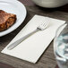 A Oneida Unity stainless steel salad/pastry fork on a napkin next to a plate of steak.
