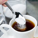 A hand holding a Oneida Unity stainless steel demitasse spoon pouring sugar into a cup of coffee.