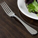 A Oneida stainless steel table fork on a plate with salad.