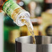 A clear plastic Acopa 0.5 oz. 3-ball measured liquor pourer dispensing liquid into a metal container.