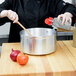A woman in a chef's uniform stirs a tomato sauce in a Vollrath Wear-Ever aluminum sauce pan on a stove.