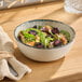 A round gray porcelain bowl filled with salad, placed on a wooden surface.