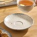 A round gray porcelain saucer with a textured surface and a slightly speckled design.
