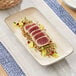 A rectangular gray porcelain platter displaying slices of seared tuna on a bed of grains with garnishes.