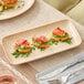A rectangular beige porcelain platter displaying three small appetizers, placed on a table setting.